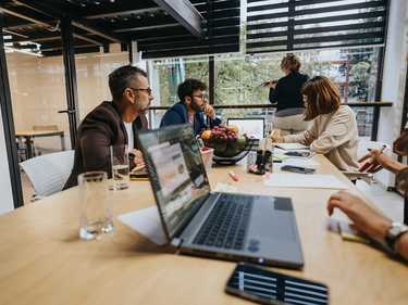 Mehrere Menschen sitzen mit Laptops an einem großen Tisch und arbeiten
